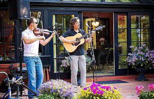 Two men play music on guitar and fiddle in the flower ladened courtyard at the best historic hotel in Cody Wyoming, the Chamberlin Inn.