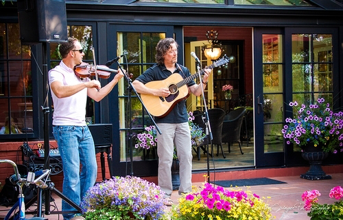 Two men play music on guitar and fiddle in the flower ladened courtyard at the best historic hotel in Cody Wyoming, the Chamberlin Inn.